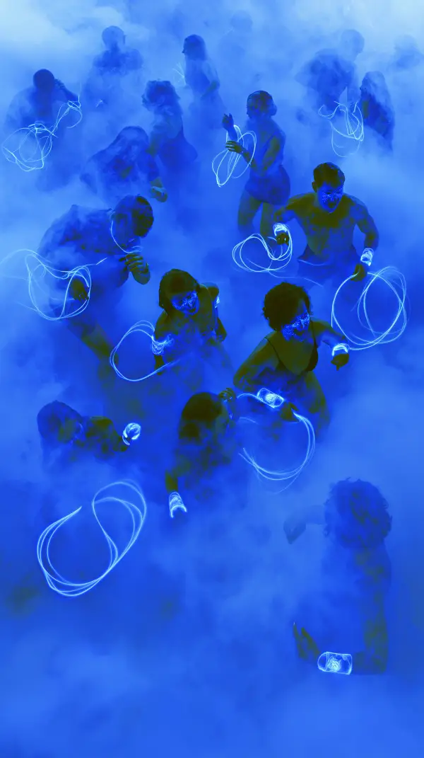 A crowd of people moves through dense blue fog wearing glowing neon wristbands that leave bright light trails in a futuristic cyberpunk scene.
