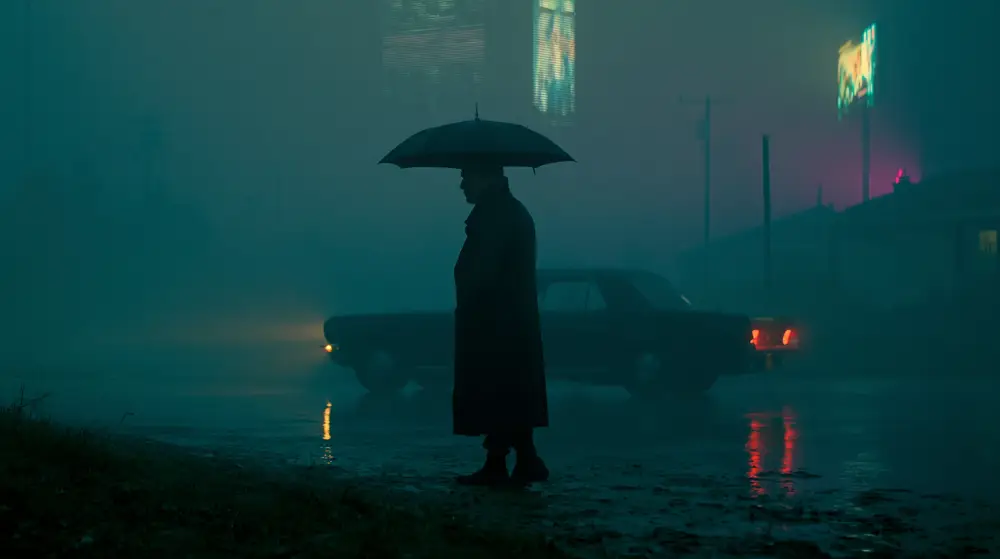 Lone umbrella figure standing beside a car on a rainy cyberpunk roadside at night.
