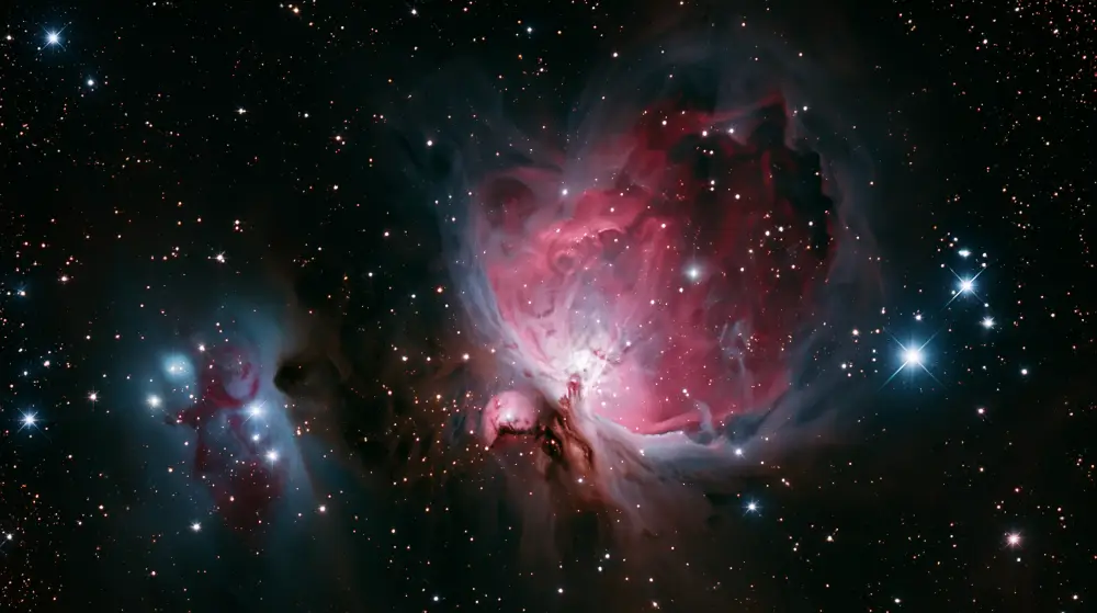 The majestic Orion Nebula glowing with vibrant pink and deep red dust clouds surrounded by bright young stars.
