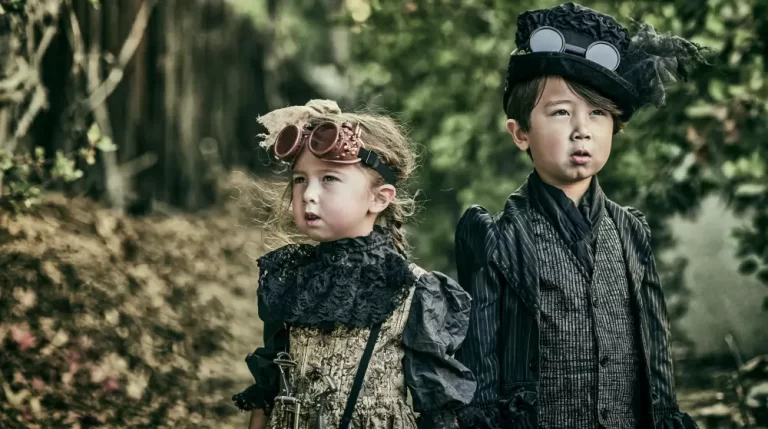 Two children wearing elegant steampunk Victorian clothing with vintage goggles stand together in a quiet forest.