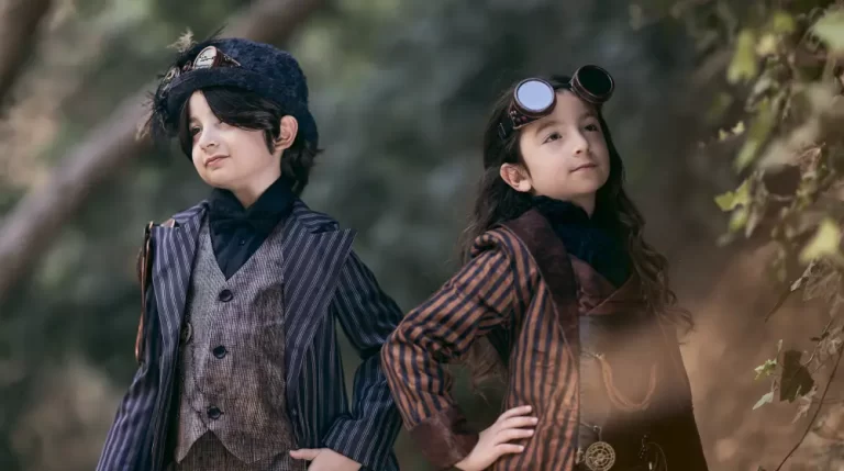 Two children wearing Victorian steampunk outfits with brass goggles pose confidently in a peaceful woodland setting.