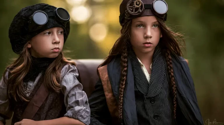 Two children wearing Victorian steampunk clothing and vintage aviator goggles pose together in a peaceful forest.