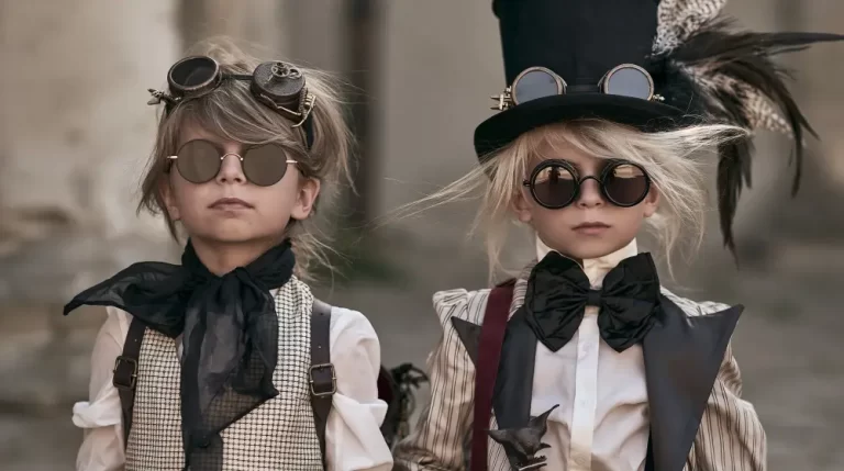 Two children wearing Victorian steampunk clothing with round goggles and a tall top hat pose for a portrait.