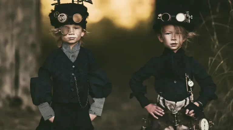 Two children wearing Victorian steampunk outfits with a monocle, clockwork headwear, and mechanical accessories pose confidently outdoors.