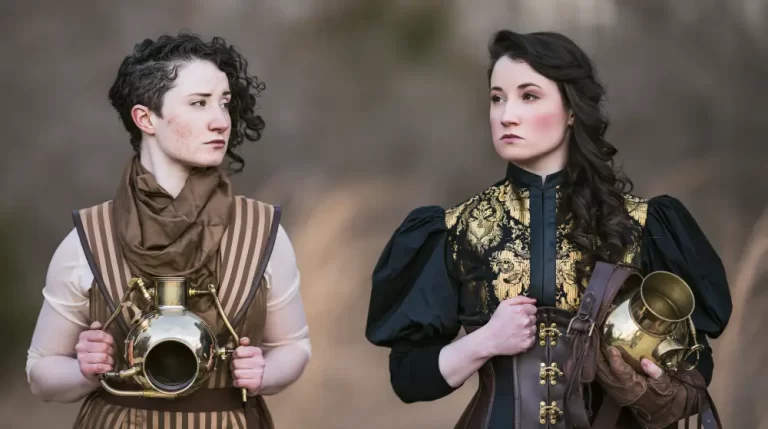 Two women wearing elegant steampunk Victorian clothing hold polished brass scientific instruments during an outdoor portrait.