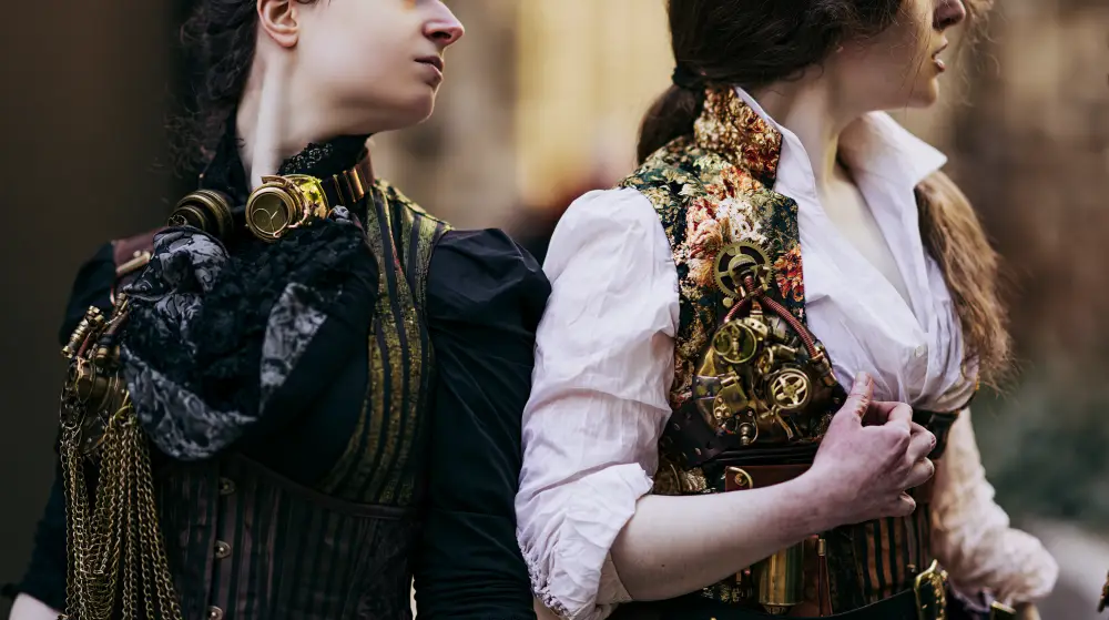Close-up of two women wearing elegant steampunk Victorian outfits with intricate mechanical corset decorations and brass accessories.