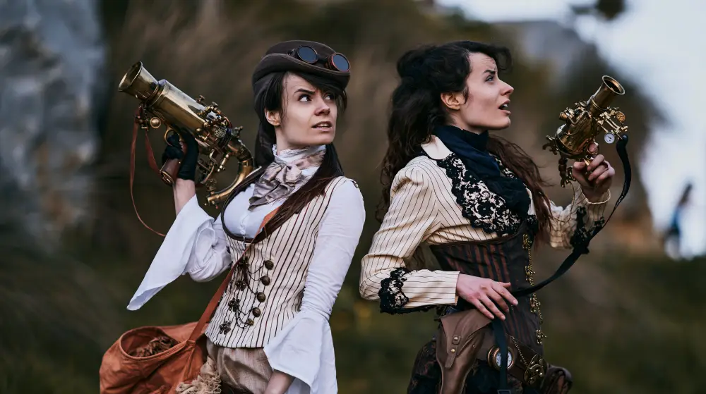 Two women in Victorian steampunk clothing hold ornate brass ray guns while scanning the landscape during an expedition.